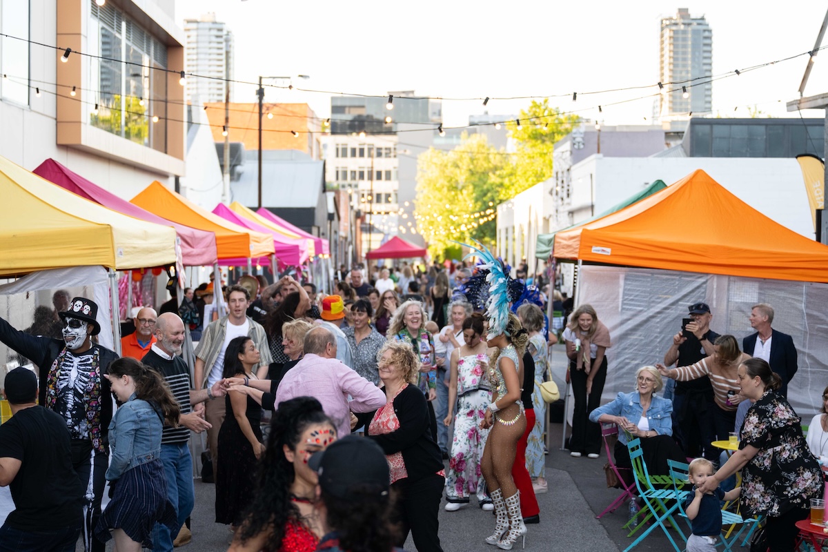Crowded Gunson Street Party in Adelaide featuring colorful market stalls, string lights, costumed performers, and dancing crowds